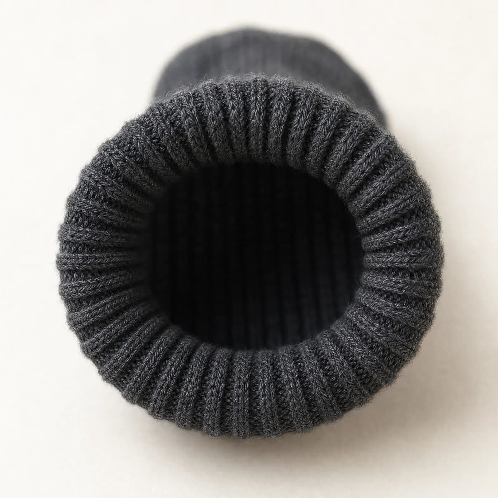 The ribbed cuff of a graphite sock at rest, its opening holding a neat even circle at its natural width.