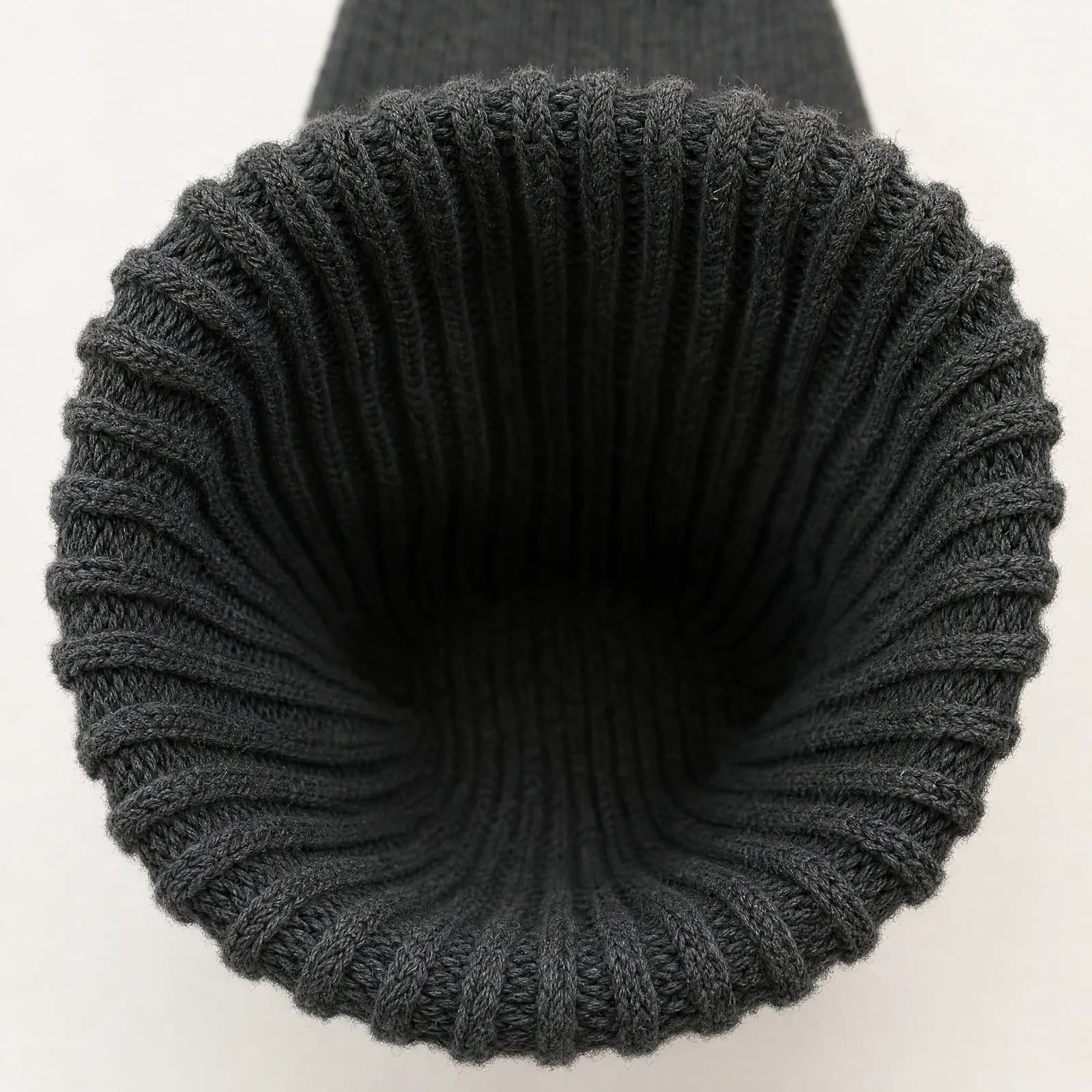 The ribbed cuff of an identical graphite sock forced open into a wide slack oval, the rib columns visibly splayed.