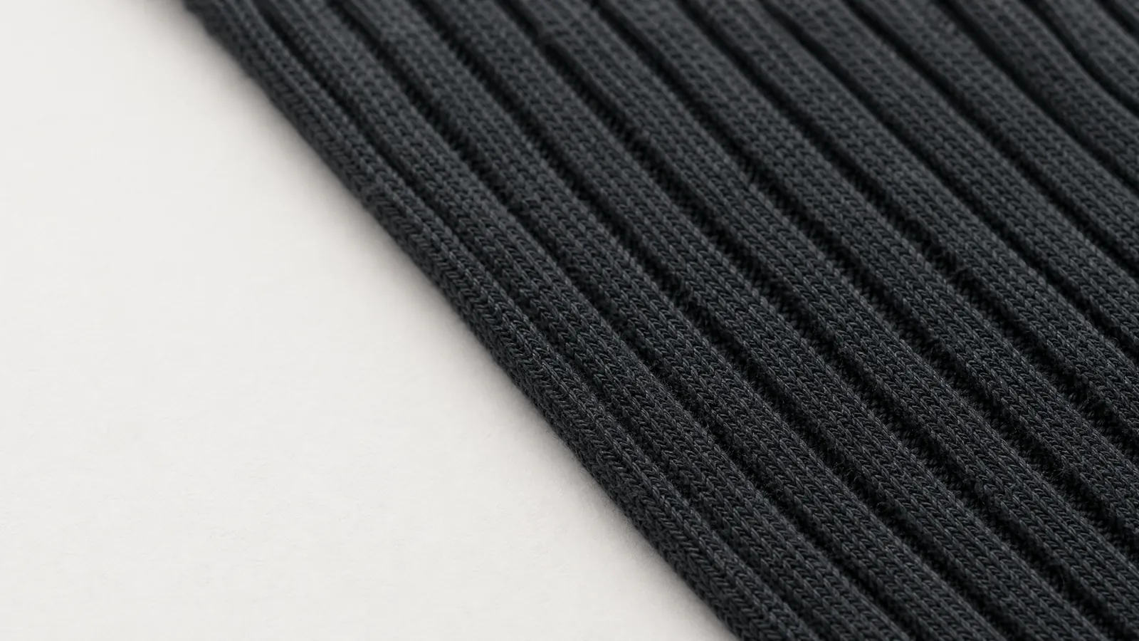 A length of graphite ribbed knit fabric laid across the frame on a strong diagonal, the rib channels running corner to corner.