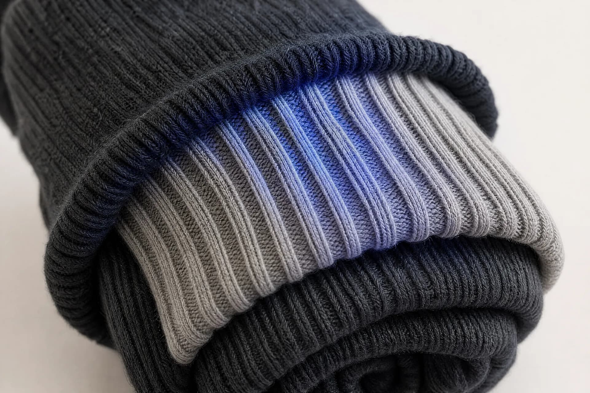 Extreme close-up of the turned-over cuff of a rolled sock bundle, its rib columns pulled apart under tension.