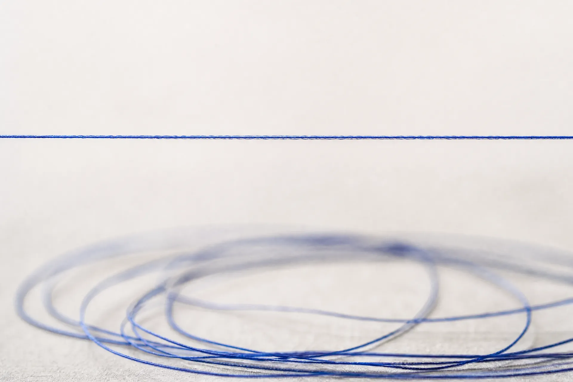 A single fine elastic filament drawn taut in a straight horizontal line, with a slack coil of the same filament resting below it.