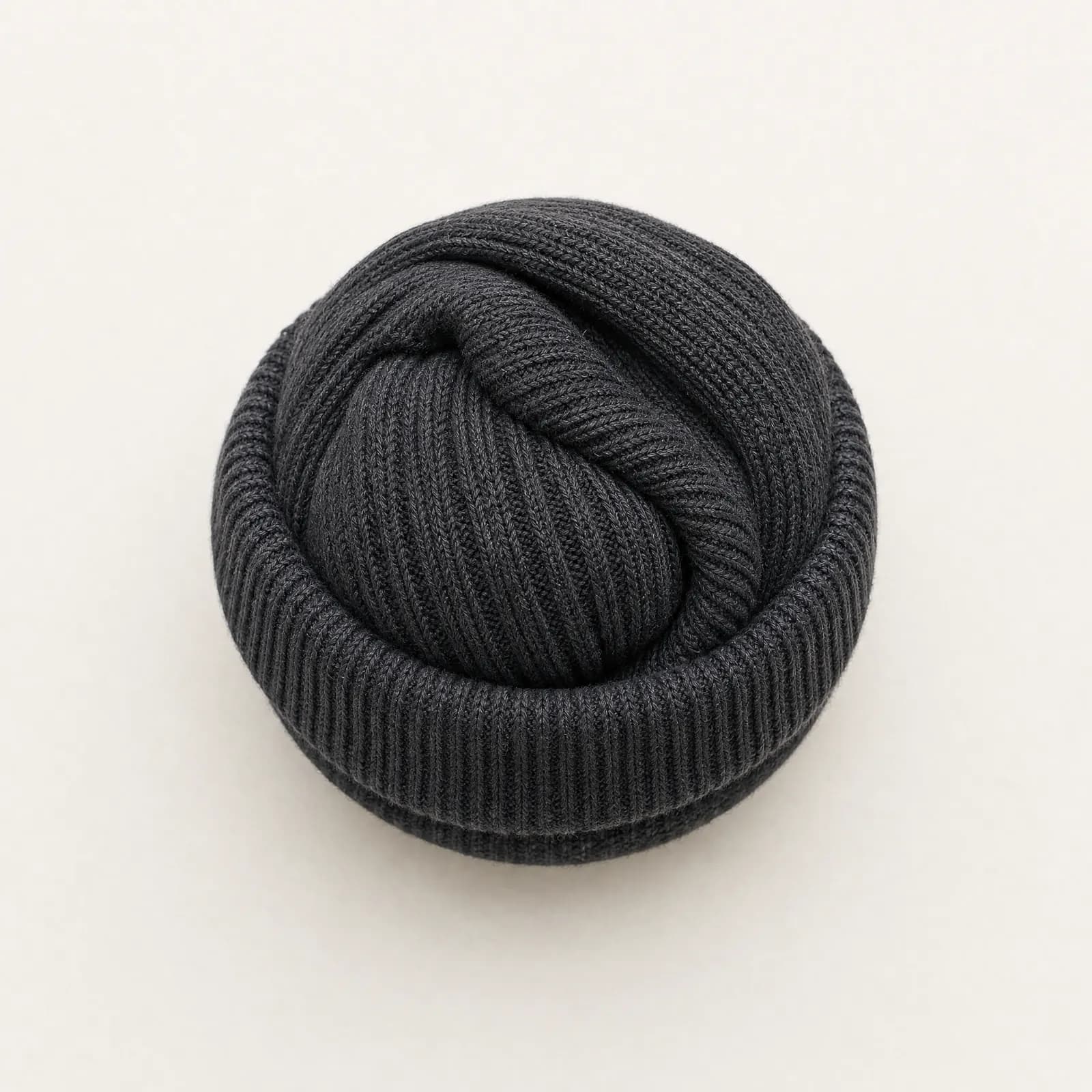 A pair of graphite ribbed socks rolled into a tight ball with one cuff turned over the bundle, the rib visibly splayed.