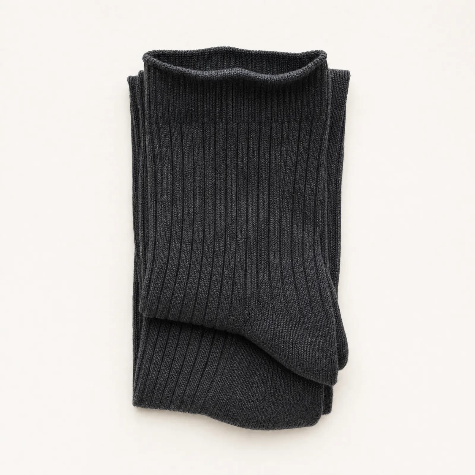 A pair of graphite ribbed socks folded once into a soft flat rectangle with the cuff turned down over the fold.