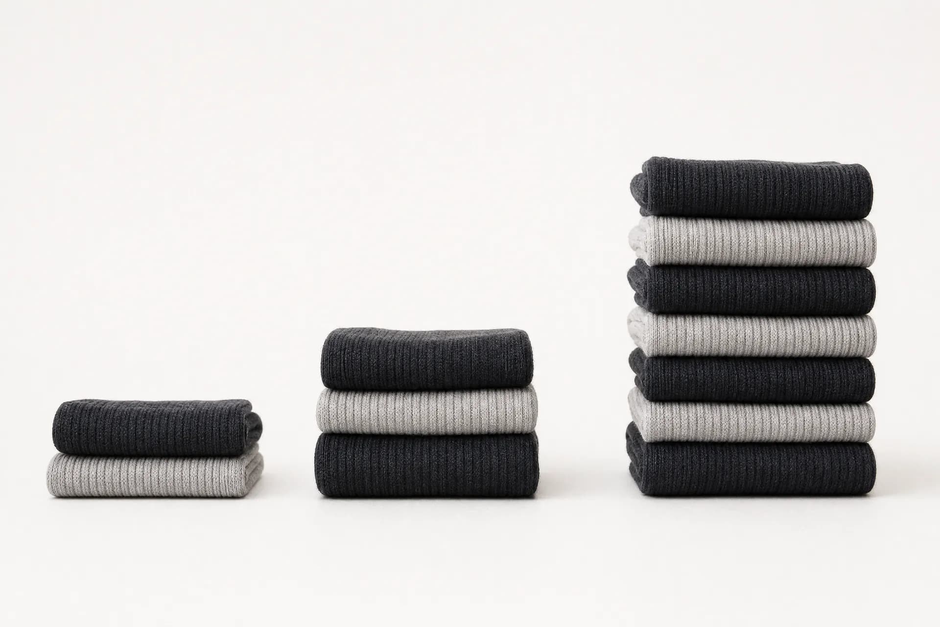 Three stacks of folded ribbed socks of increasing height standing in a row against a plain background.