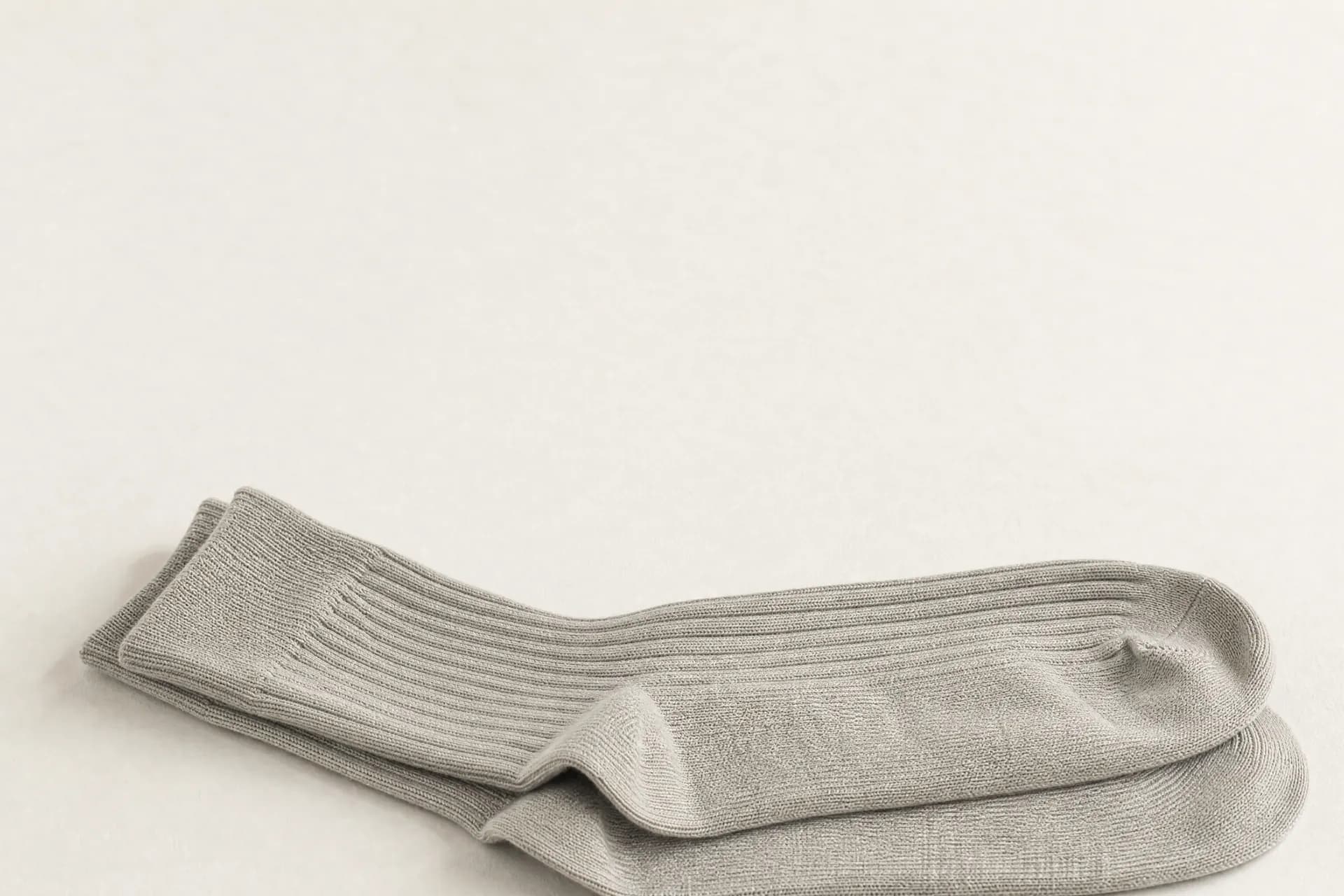 A pair of pale rib grey ribbed socks laid flat and slightly overlapping against a plain warm off-white background.